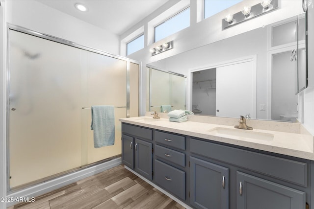 full bathroom featuring double vanity, a stall shower, wood finished floors, and a sink