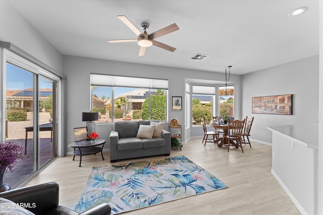 living area featuring visible vents, baseboards, light wood-style floors, and ceiling fan