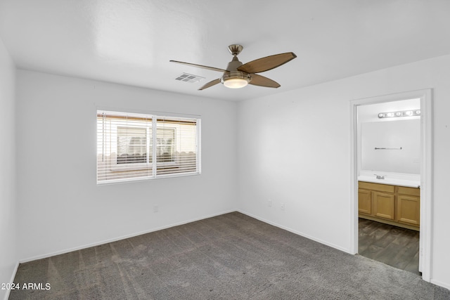 unfurnished bedroom with ceiling fan, sink, dark colored carpet, and ensuite bath