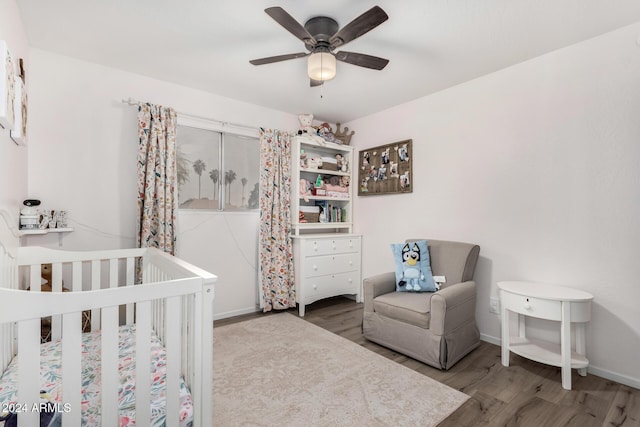 bedroom with a nursery area, hardwood / wood-style flooring, and ceiling fan