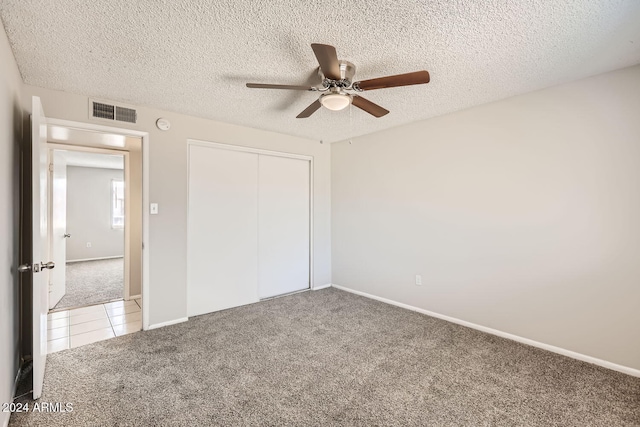 unfurnished bedroom featuring light colored carpet, a textured ceiling, a closet, and ceiling fan