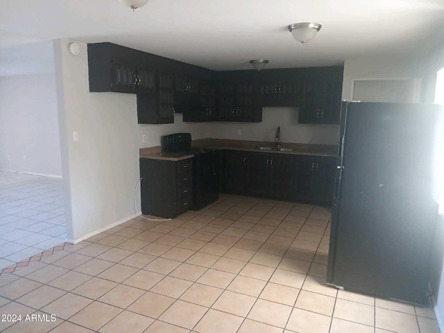 kitchen featuring refrigerator, sink, black range oven, and light tile patterned floors