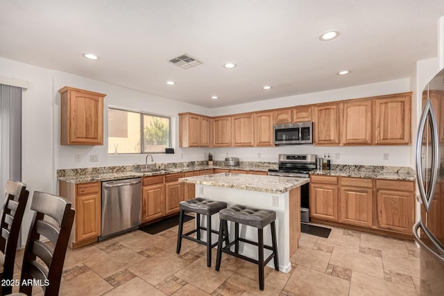 kitchen featuring light stone counters, appliances with stainless steel finishes, a center island, and a breakfast bar area