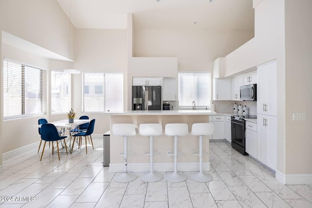 kitchen featuring a breakfast bar, stainless steel appliances, sink, a center island, and white cabinetry