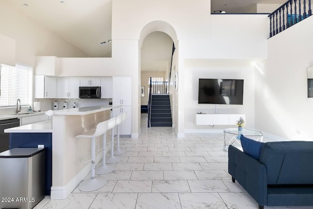 kitchen featuring a kitchen bar, backsplash, sink, high vaulted ceiling, and white cabinetry