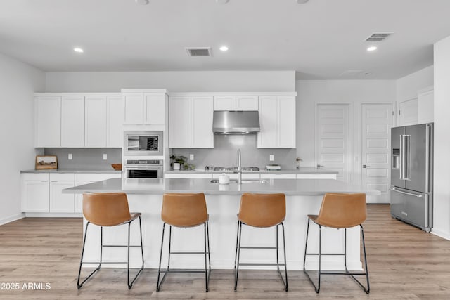 kitchen with an island with sink, appliances with stainless steel finishes, white cabinets, and light wood-type flooring