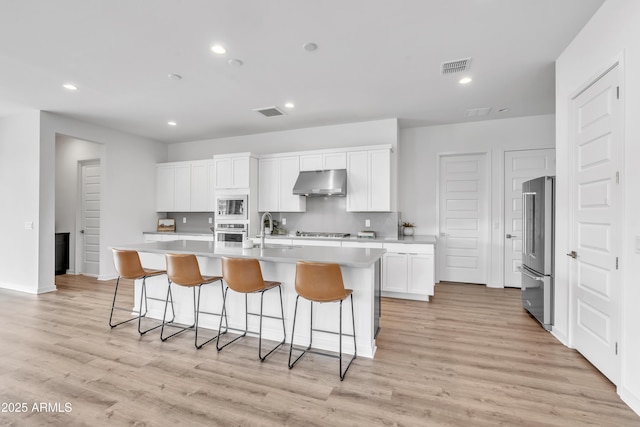 kitchen with appliances with stainless steel finishes, white cabinetry, an island with sink, sink, and light hardwood / wood-style flooring