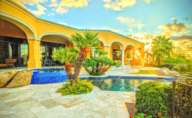 pool at dusk with a patio area and an in ground hot tub