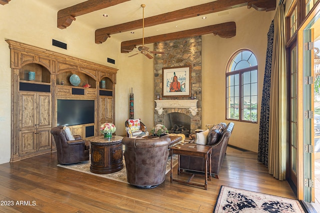 living room featuring a towering ceiling, ceiling fan, beam ceiling, hardwood / wood-style flooring, and a fireplace