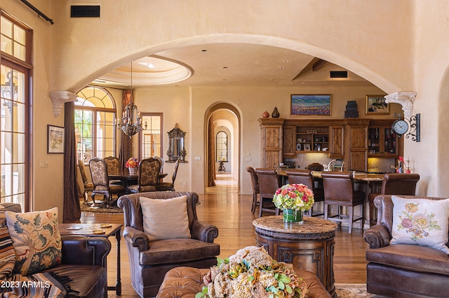 living room with a chandelier, light wood-type flooring, and a raised ceiling