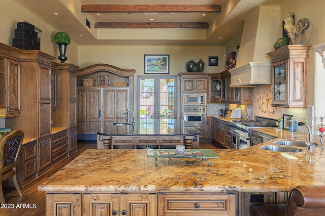 kitchen with beamed ceiling, dark hardwood / wood-style flooring, light stone counters, and stainless steel appliances