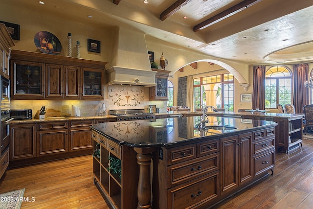 kitchen featuring sink, hardwood / wood-style flooring, custom exhaust hood, and an island with sink