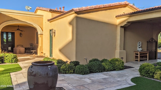 view of exterior entry featuring ceiling fan and a patio