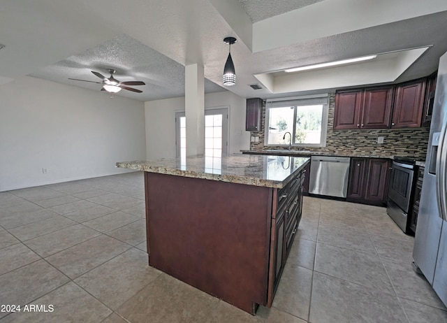 kitchen featuring sink, a raised ceiling, light stone counters, pendant lighting, and appliances with stainless steel finishes