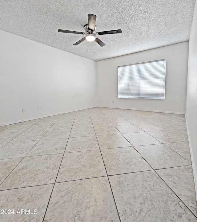 empty room with ceiling fan, light tile patterned floors, and a textured ceiling