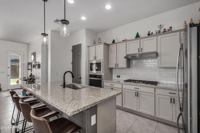 kitchen with light stone countertops, stainless steel appliances, a kitchen island with sink, sink, and hanging light fixtures