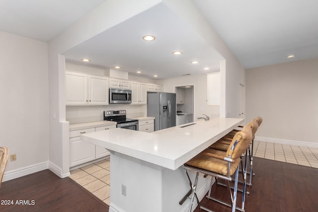 kitchen with sink, white cabinets, kitchen peninsula, a kitchen breakfast bar, and stainless steel appliances