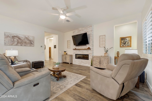 living room featuring ceiling fan, hardwood / wood-style flooring, a healthy amount of sunlight, and a stone fireplace