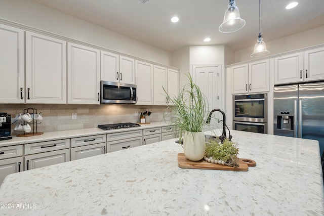 kitchen with hanging light fixtures, white cabinetry, light stone counters, tasteful backsplash, and stainless steel appliances