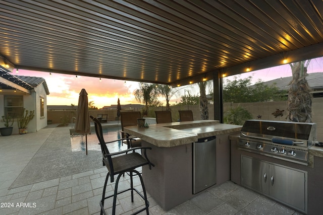 patio terrace at dusk featuring exterior kitchen, exterior bar, and grilling area