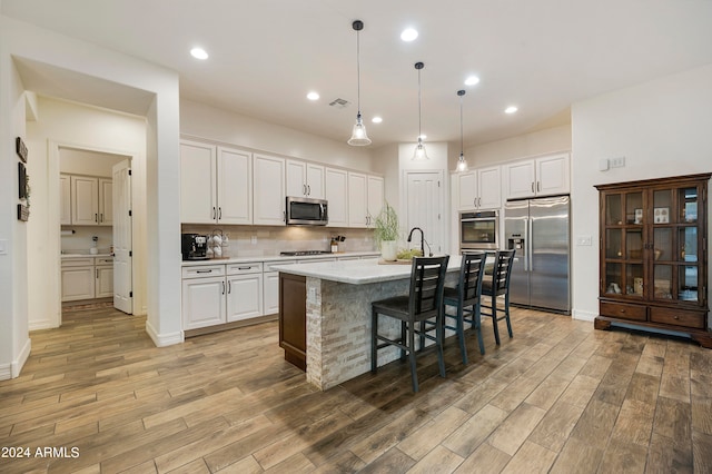 kitchen with a kitchen island with sink, stainless steel appliances, light wood-type flooring, and white cabinetry