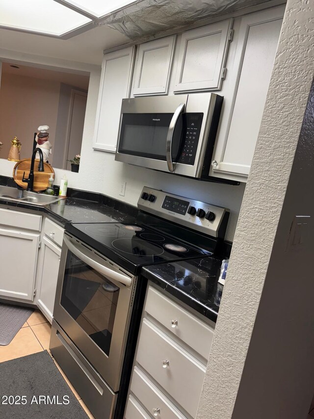 9060 N 47th Ln, Glendale, AZ 85302 - kitchen with appliances with stainless steel finishes, dark countertops, light tile patterned floors, a sink, and white cabinets