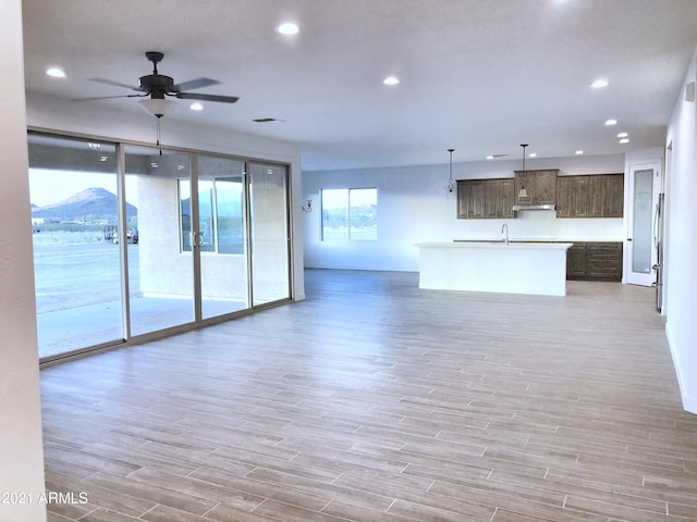 unfurnished living room featuring ceiling fan, sink, light hardwood / wood-style floors, and a mountain view