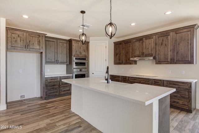 kitchen featuring pendant lighting, black electric cooktop, hardwood / wood-style floors, stainless steel double oven, and a kitchen island with sink