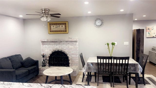 dining room featuring a fireplace, wood-type flooring, and ceiling fan