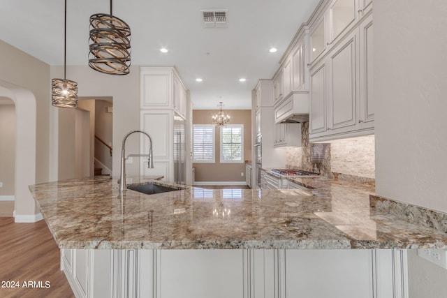 kitchen with tasteful backsplash, sink, hanging light fixtures, kitchen peninsula, and light stone countertops