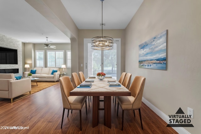 dining area with hardwood / wood-style flooring, a stone fireplace, and ceiling fan with notable chandelier