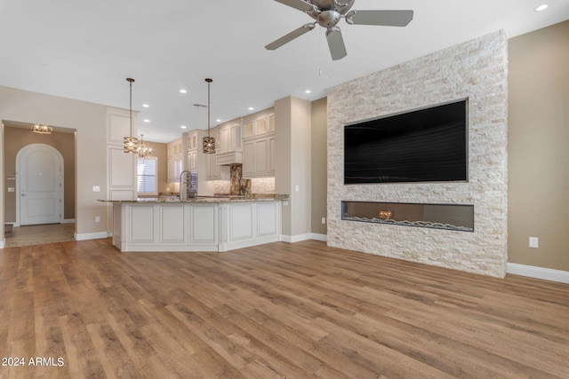 unfurnished living room with ceiling fan with notable chandelier, a stone fireplace, light hardwood / wood-style floors, and sink