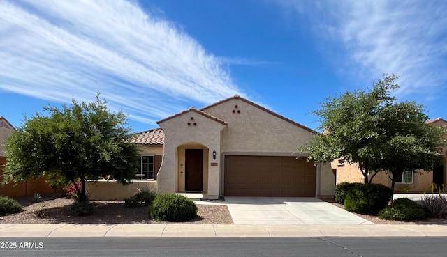 mediterranean / spanish house featuring concrete driveway, a garage, stucco siding, and a tiled roof