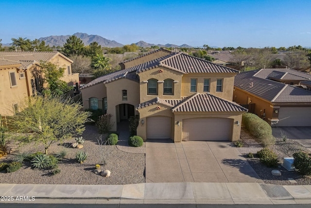 mediterranean / spanish house featuring a garage, concrete driveway, a tiled roof, a mountain view, and stucco siding