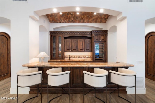 bar featuring wood-type flooring, vaulted ceiling, and brick ceiling