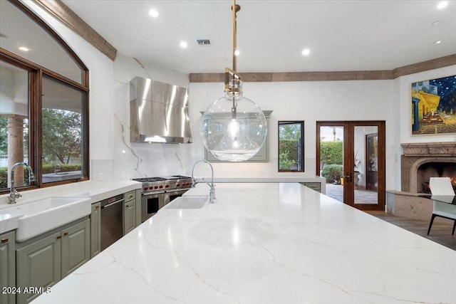 kitchen featuring sink, light stone countertops, wall chimney range hood, and plenty of natural light