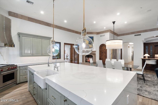 kitchen with hanging light fixtures, sink, a center island with sink, and premium stove