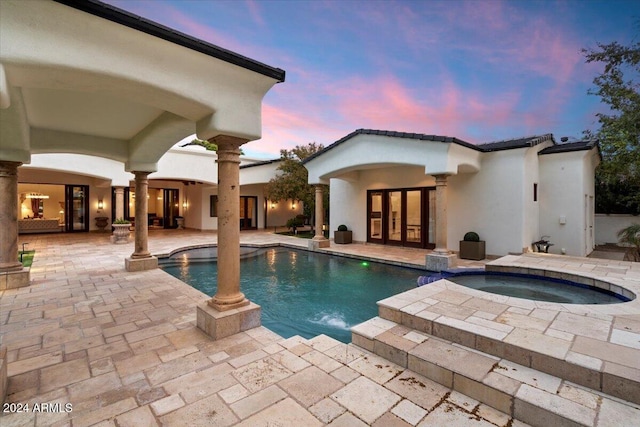 pool at dusk with a patio, french doors, pool water feature, and an in ground hot tub