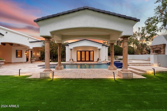 back house at dusk with a patio, an outdoor stone fireplace, and a yard