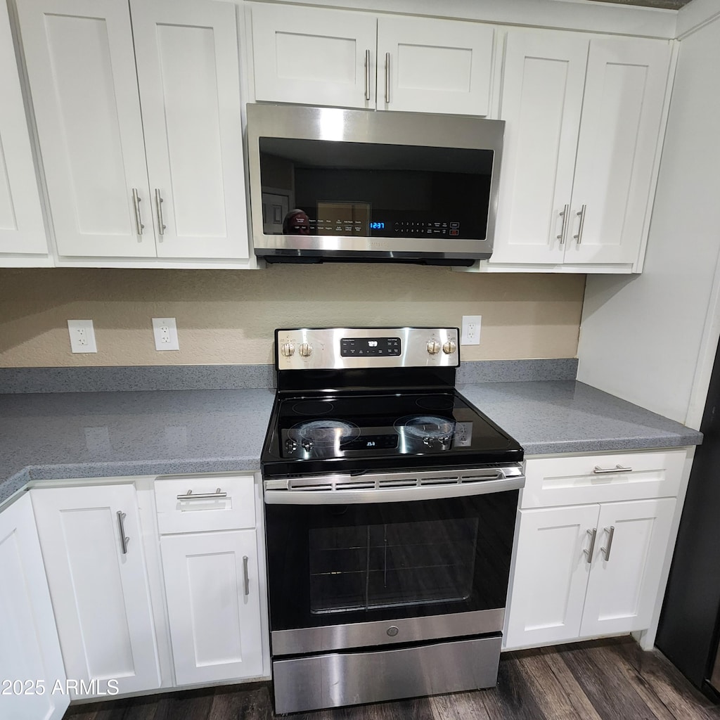 kitchen with dark wood-type flooring, appliances with stainless steel finishes, and white cabinetry