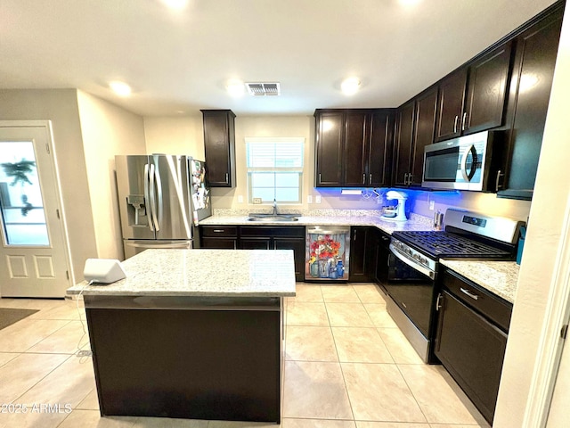 kitchen with sink, light tile patterned floors, stainless steel appliances, light stone countertops, and a kitchen island