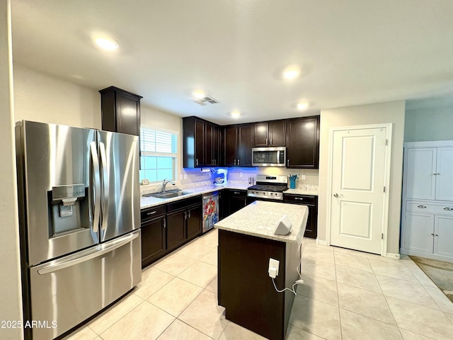 kitchen featuring sink, light tile patterned floors, stainless steel appliances, dark brown cabinetry, and a kitchen island