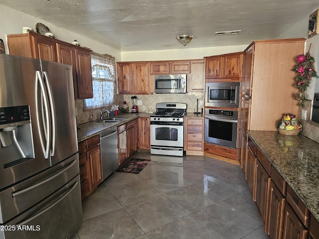 kitchen featuring dark stone countertops, sink, backsplash, and appliances with stainless steel finishes