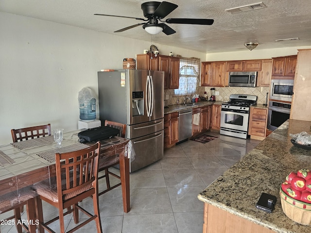 kitchen featuring sink, stainless steel appliances, tasteful backsplash, light stone countertops, and tile patterned floors