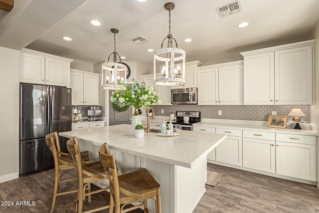 kitchen featuring tasteful backsplash, stainless steel appliances, a kitchen island with sink, pendant lighting, and white cabinetry