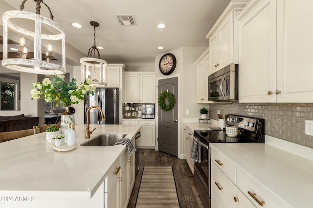 kitchen with sink, hanging light fixtures, stainless steel appliances, tasteful backsplash, and a center island with sink