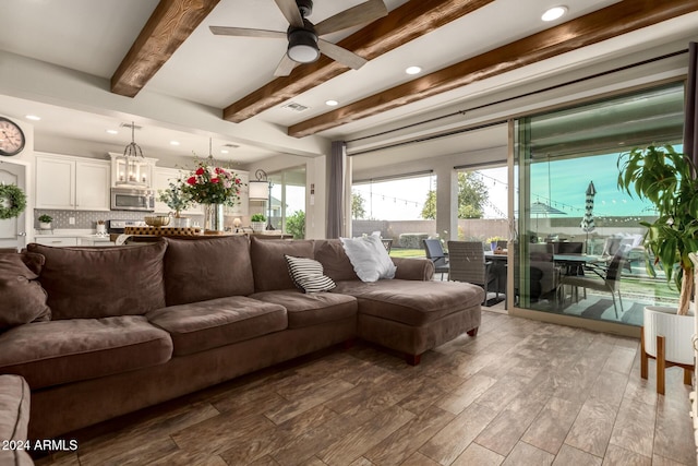 living room featuring ceiling fan with notable chandelier, beam ceiling, and light hardwood / wood-style floors