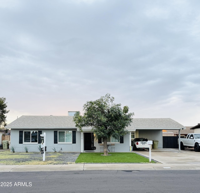 ranch-style house with a carport, concrete driveway, a shingled roof, and a front yard