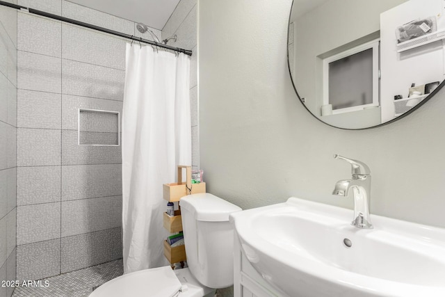 bathroom featuring toilet, a tile shower, and a sink