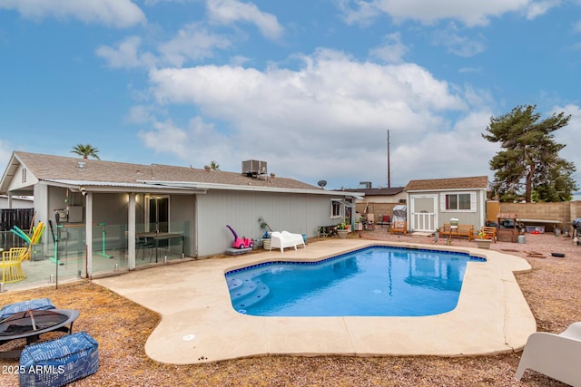 view of swimming pool featuring an outbuilding, a patio, an outdoor fire pit, a fenced backyard, and central air condition unit